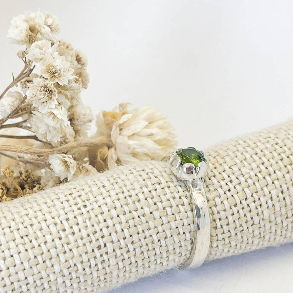 Handcrafted sterling silver stacking ring set with a 5mm green peridot stone on a textured band, presented against a natural fabric background.