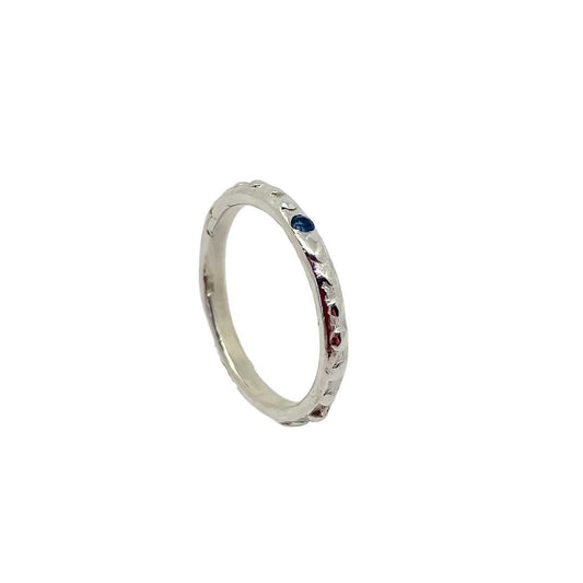 Fluid Nova Stacking Ring in sterling silver with a flush-set natural blue sapphire, standing upright with sapphire visible and the inside of the band showing, viewed from the top right.