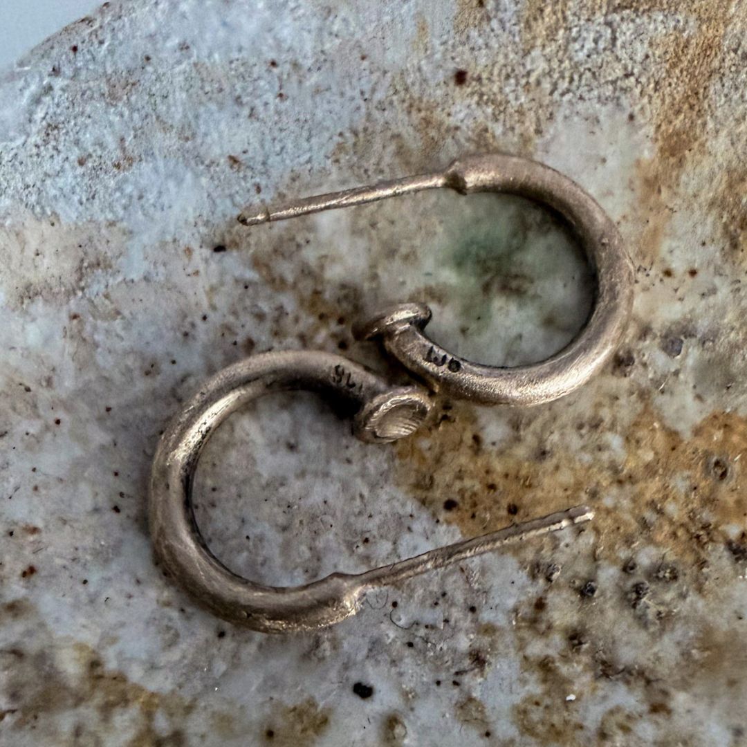A pair of small 9ct gold hoop earrings with post backs, displayed on a textured, speckled stone surface.