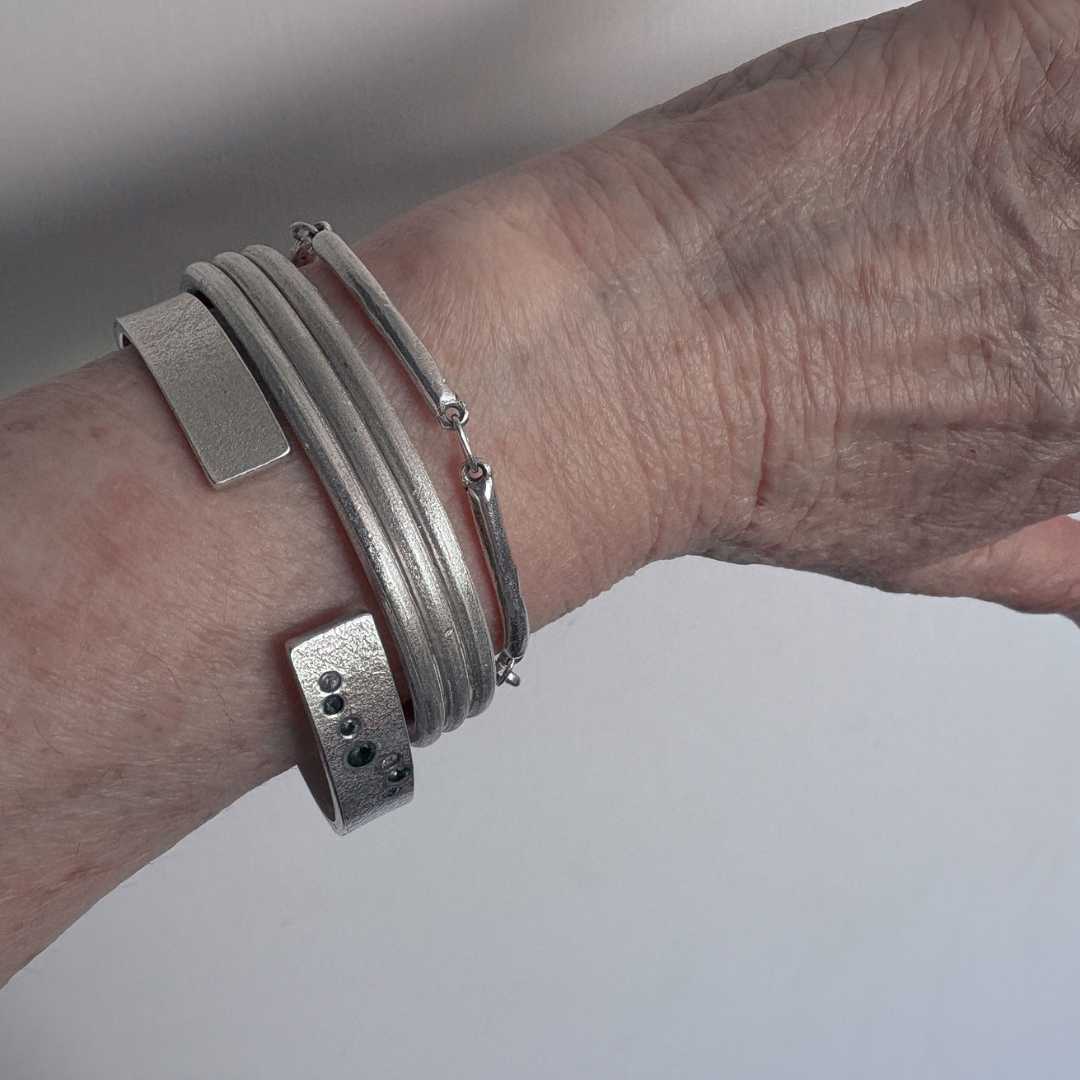 Three Line Cuff worn alongside a bespoke sterling silver and sapphire cuff and the Line Chain Bracelet, showing scale, proportion, and how the pieces stack together.