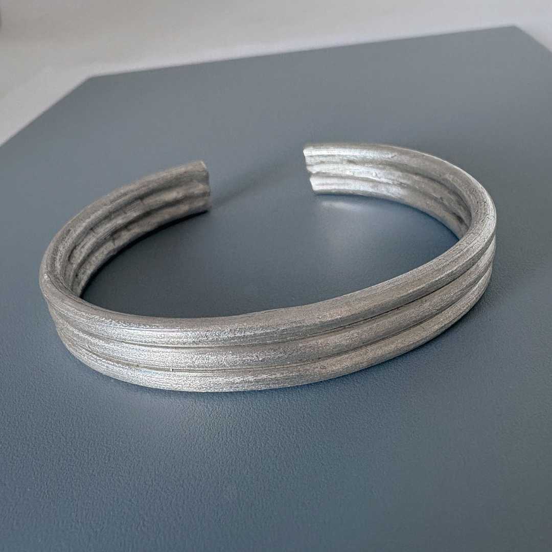 Three Line Cuff in sterling silver photographed from a slightly elevated right angle, showing the front three lines, the back opening, and part of the interior detailing on a steel-blue board with a light grey border.