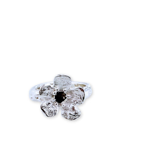 Front view of Waiatarua Narrow sterling silver flower ring with textured petals and a dark blue sapphire centre.