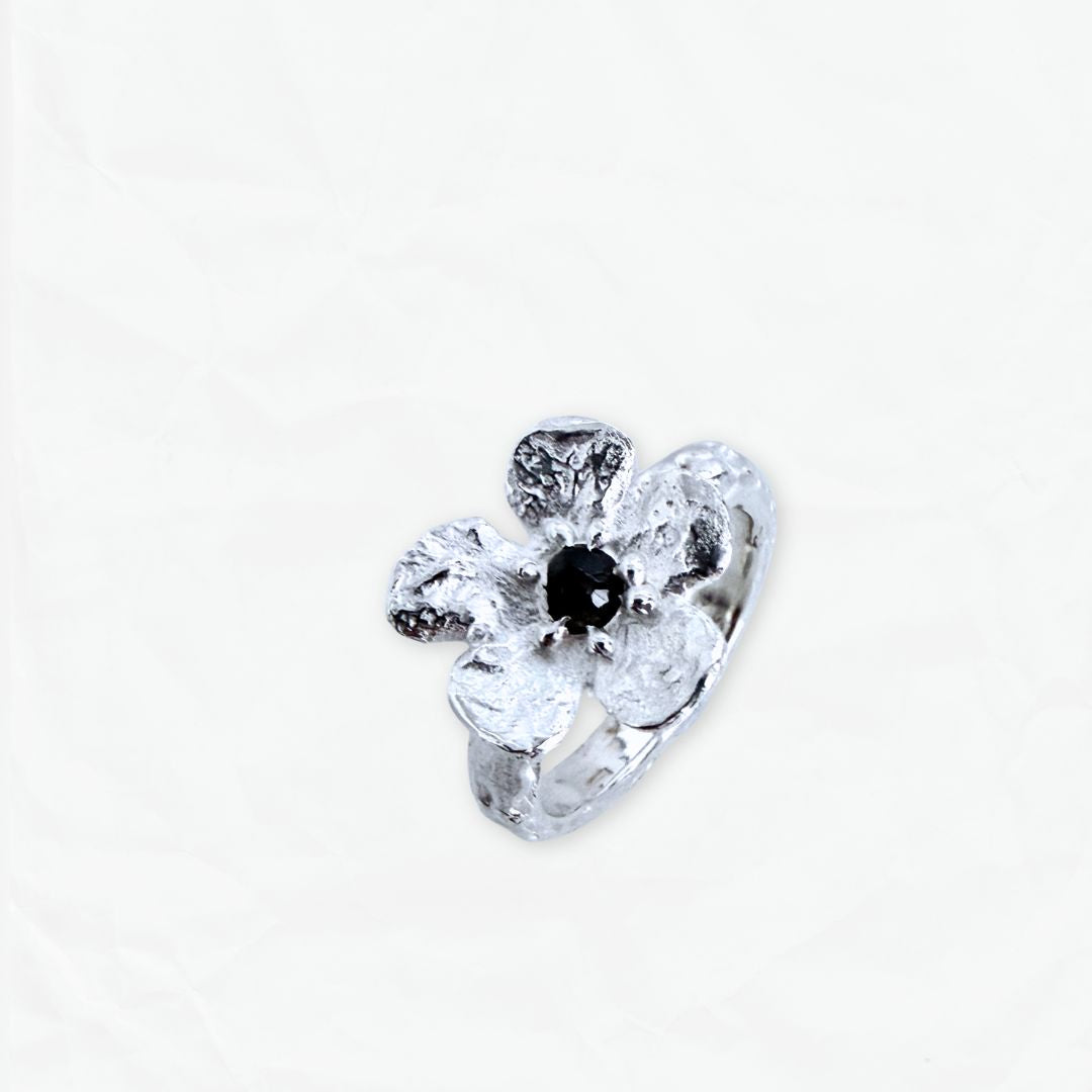 Angled view of Waiatarua Narrow flower ring showing the slim textured silver band and dark blue sapphire.