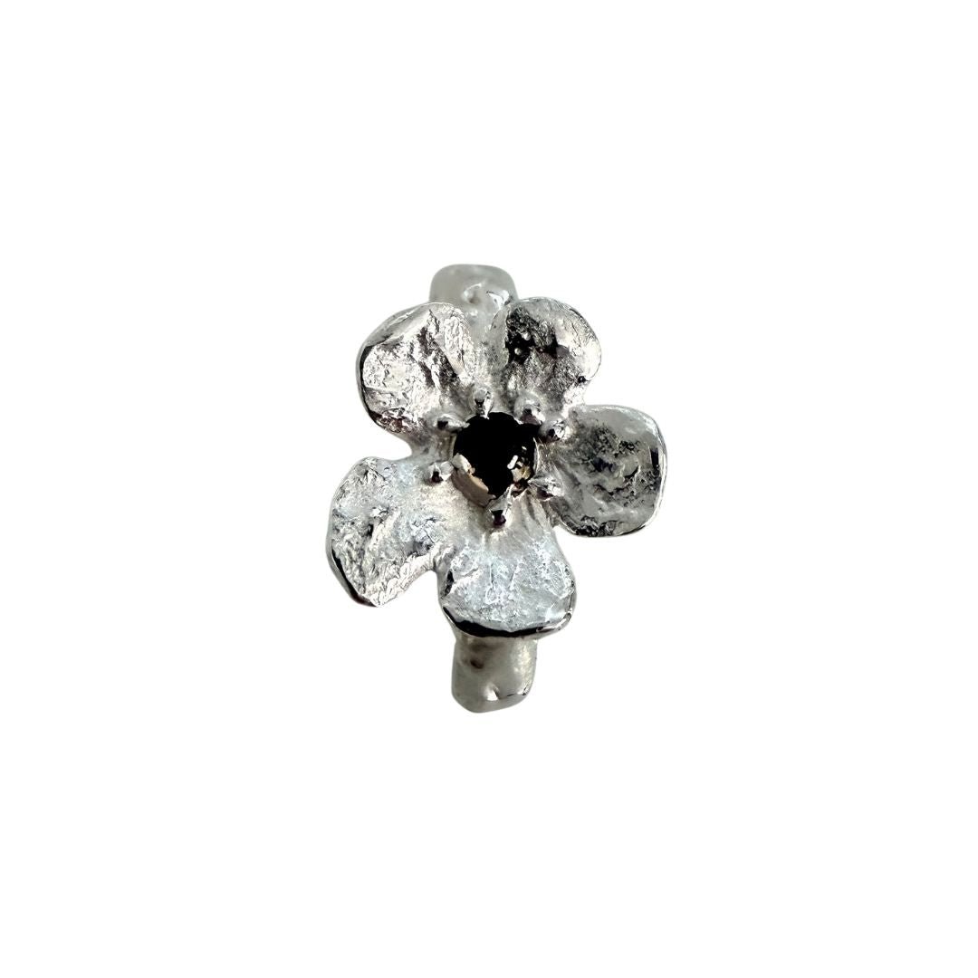 Close-up of Waiatarua Narrow flower ring showing irregular sculpted silver petals and a dark blue sapphire centre.