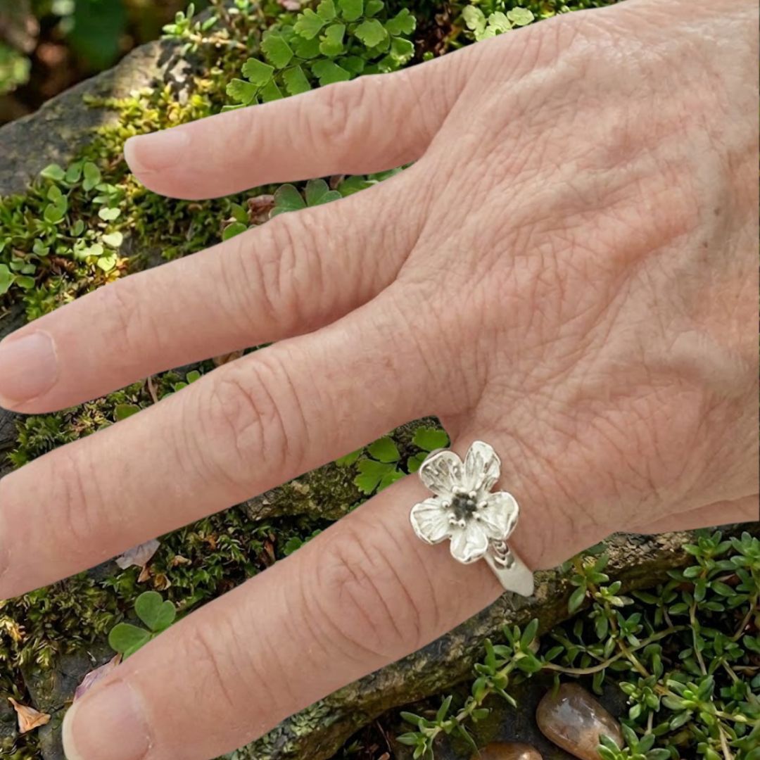 Waiatarua Narrow blue sapphire flower ring worn on the hand, showing the scale of the 15mm flower and slim silver band.