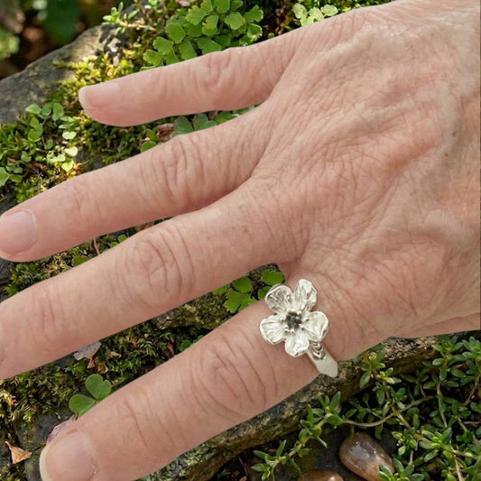 Waiatarua Narrow blue sapphire flower ring worn on the hand, showing the scale of the 15mm flower and slim silver band.