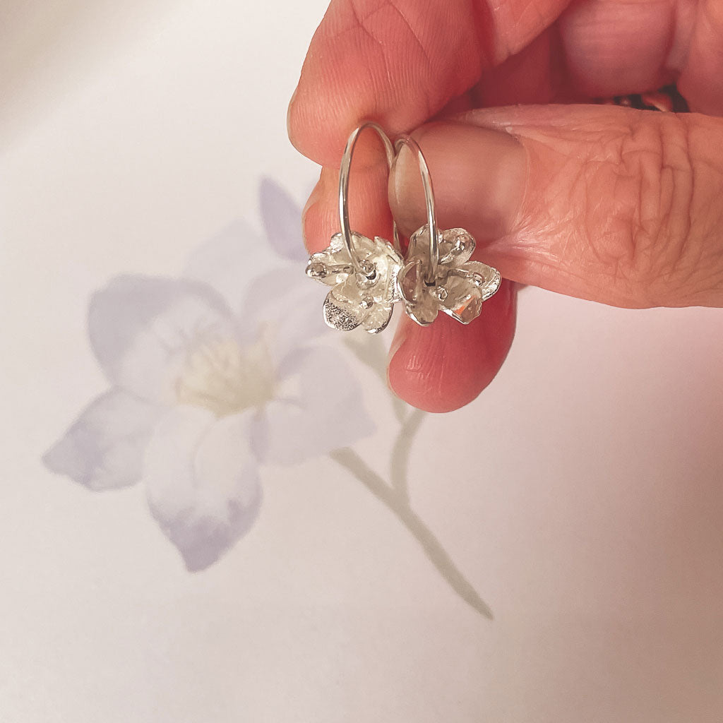 A hand holding a pair of delicate 3D Sterling Silver freesia Flower Hoop Earrings