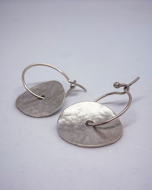A closeup of a pair of discs of Sterling Silver that sits on a hoop earring