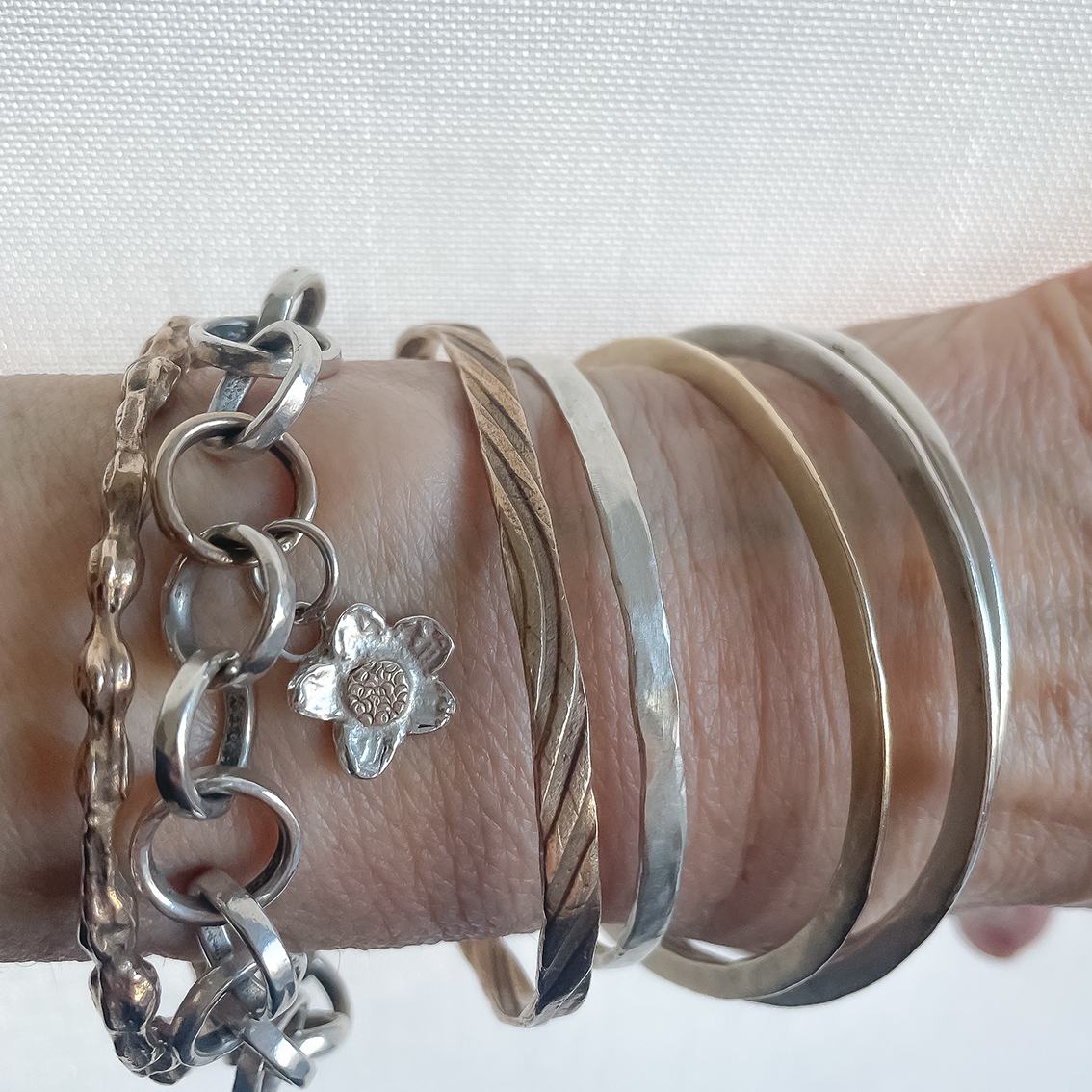 Arm showing a collection of Bangles and Chains in Silver, Gold and Bronze