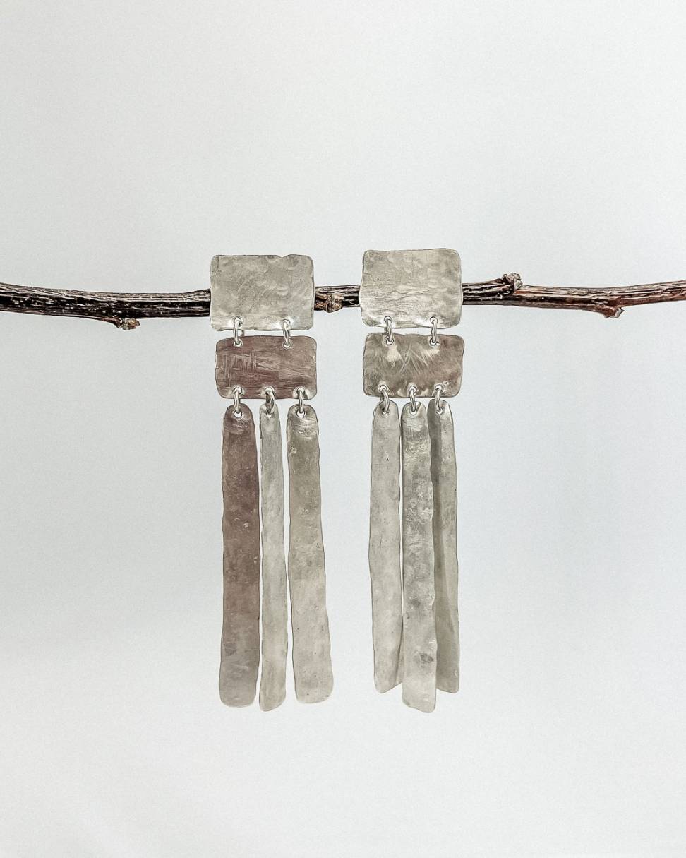 A close up of Long silver earrings hung from a branch . Each earring formed from five Geometric forms