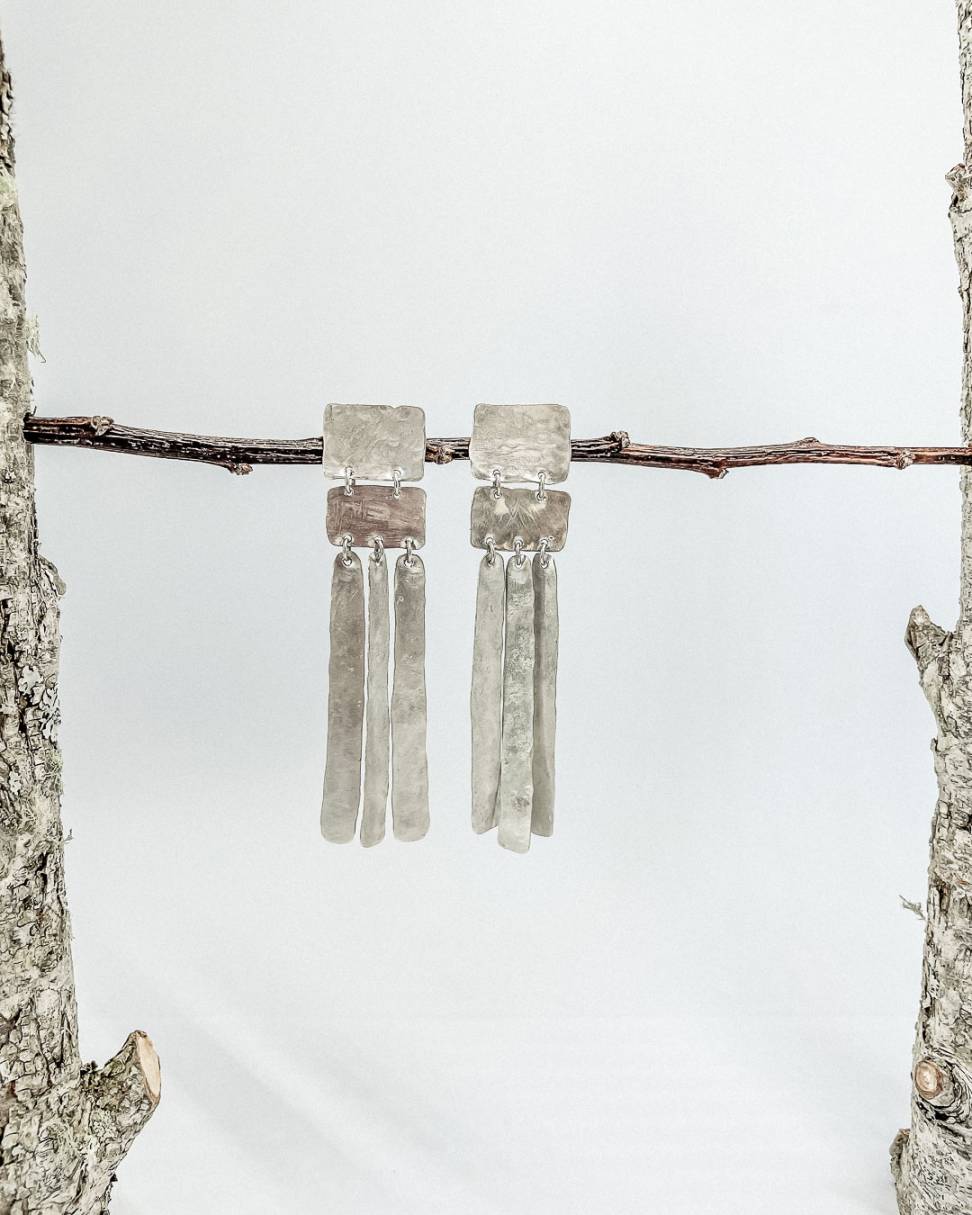 Long silver earrings hung from a branch . Each earring formed from five Geometric forms