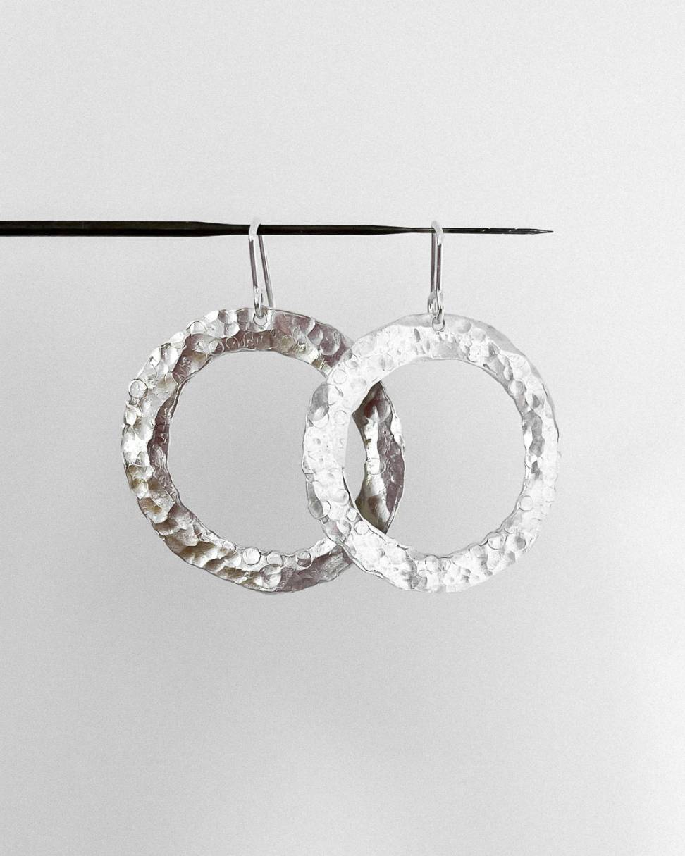 Front view of a pair of Sterling Silver textured Circle Hoop Earrings hanging from a felting needle