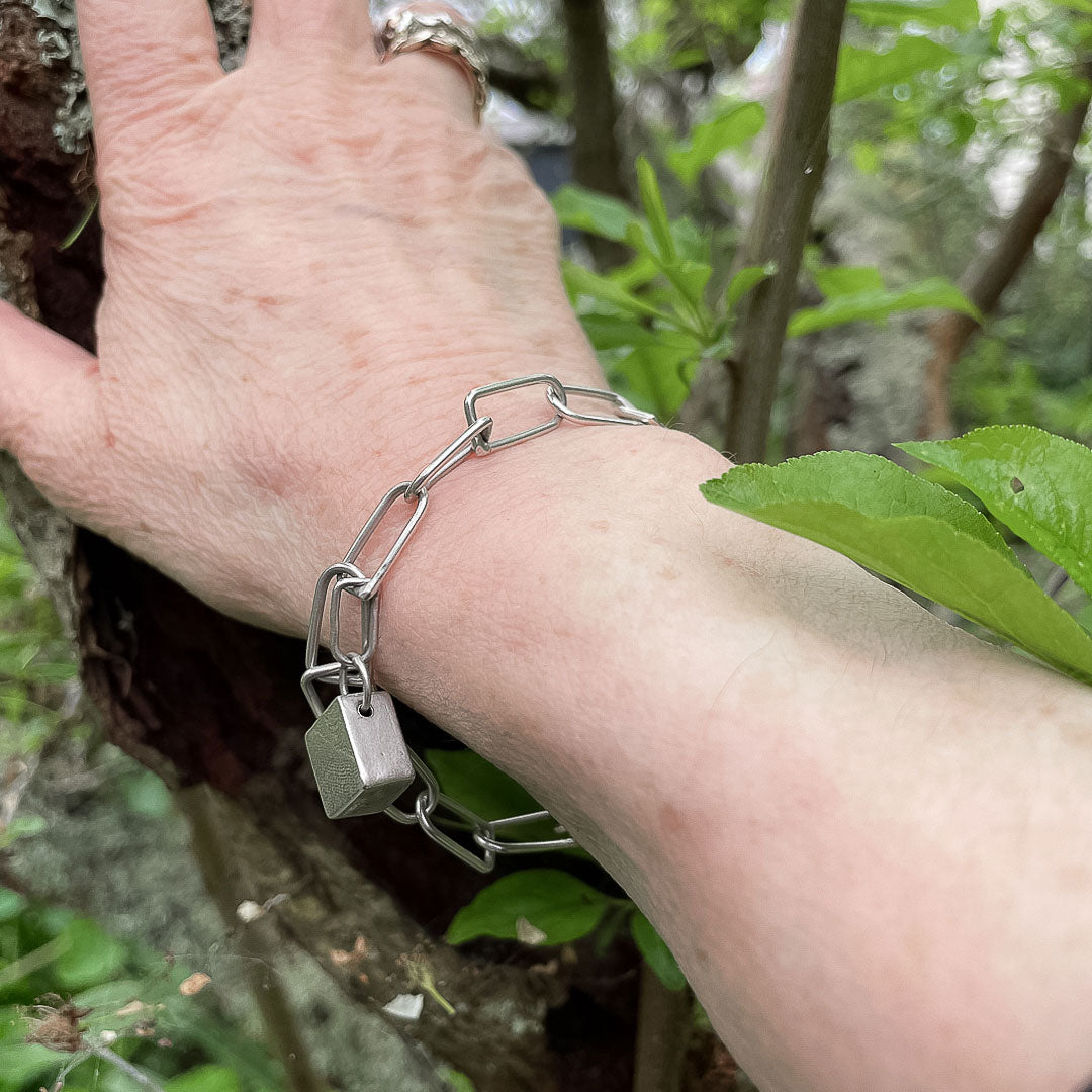 A hand resting against a branch showing the D Link Bracelet Chain being worn