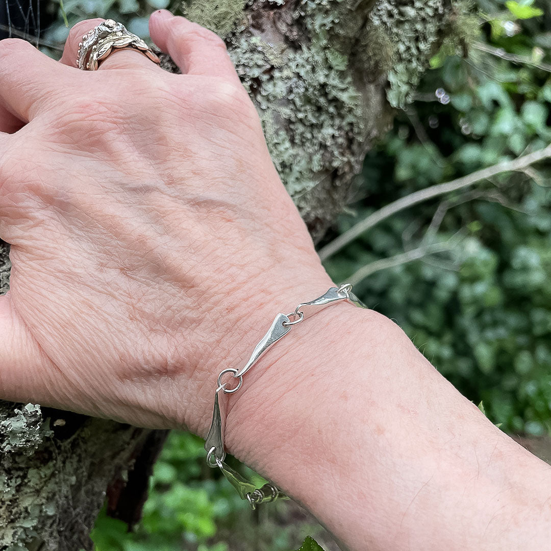 A hand resting against a branch showing the Modernist Butterfly Link Chain Bracelet being worn