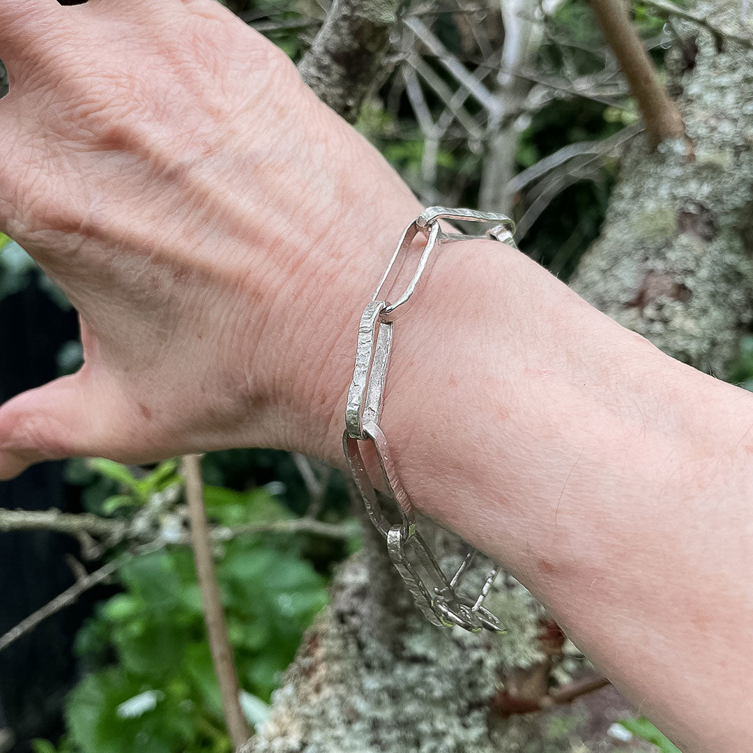 A hand resting against a branch showing the Heavy textured Oval Link Chain Bracelet being worn