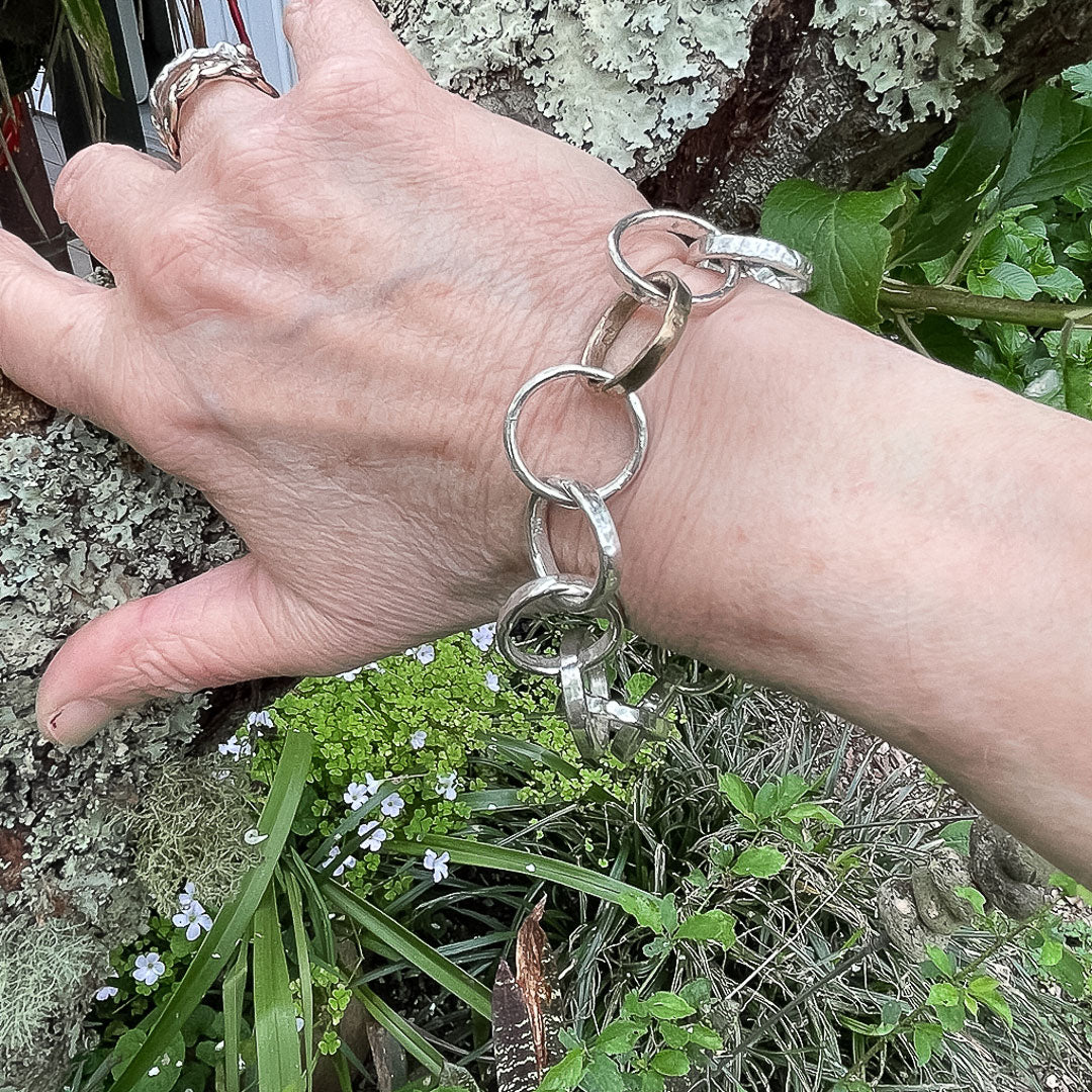 A hand resting against a branch showing the Heavy organic circle Chain Bracelet being worn