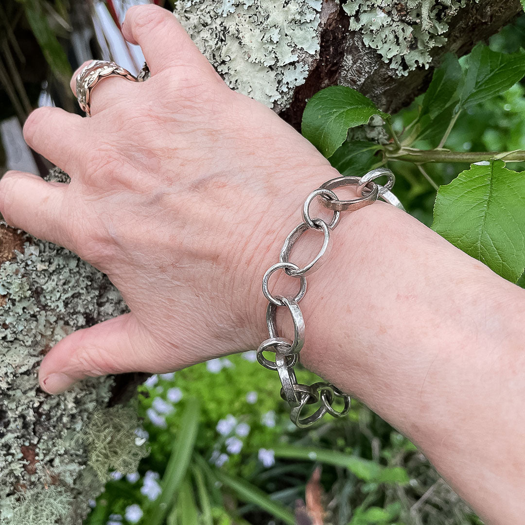 A hand resting against a branch showing the Pattern Chain Bracelet being worn