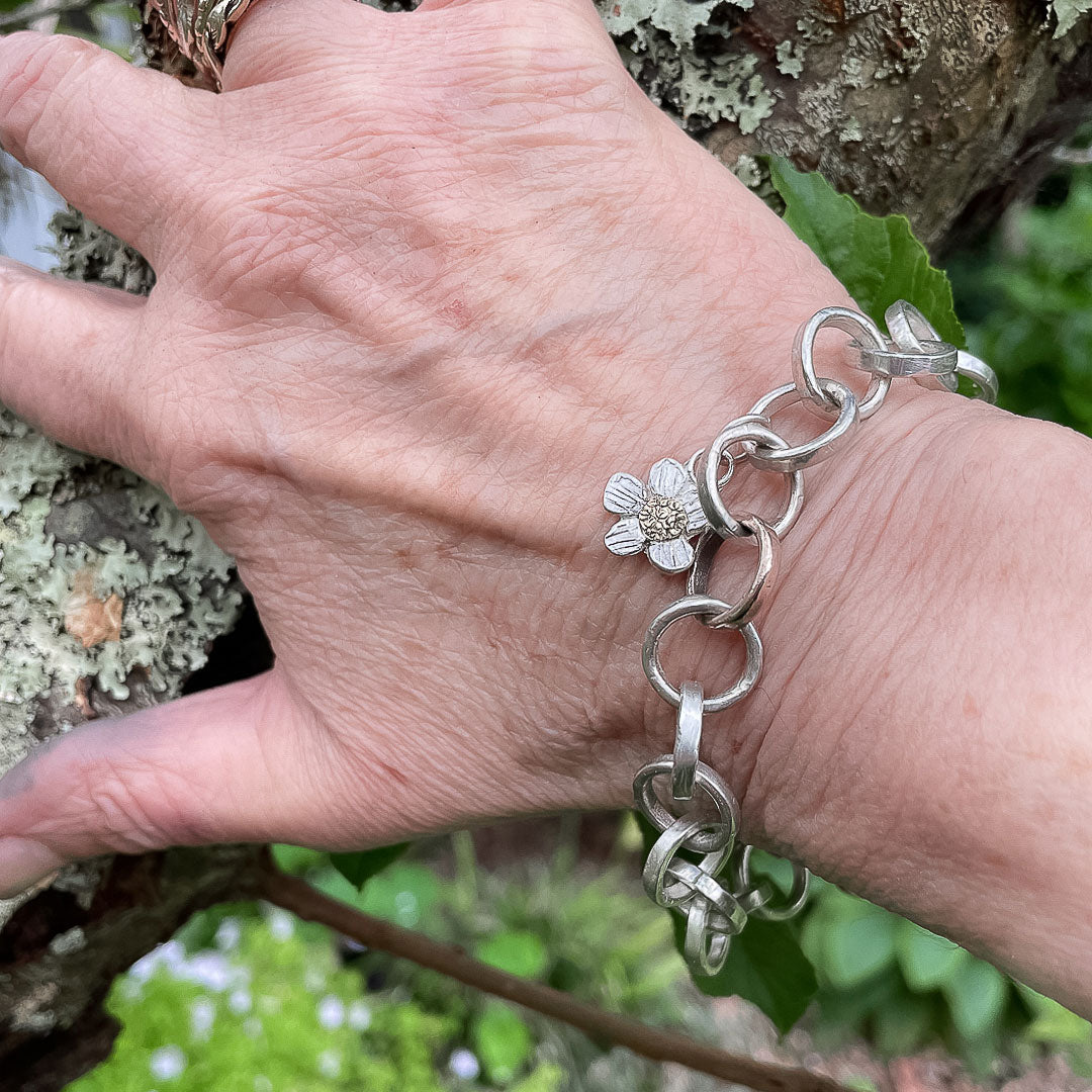 A hand resting against a branch showing the Elixir Chain Bracelet with Alpine Daisy charm being worn