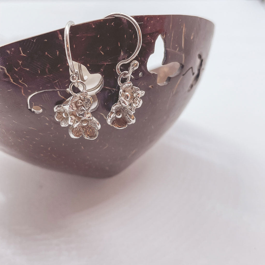 a pair of floral silver earrings hanging from a delicate wooden bowl that has butterflies cut out
