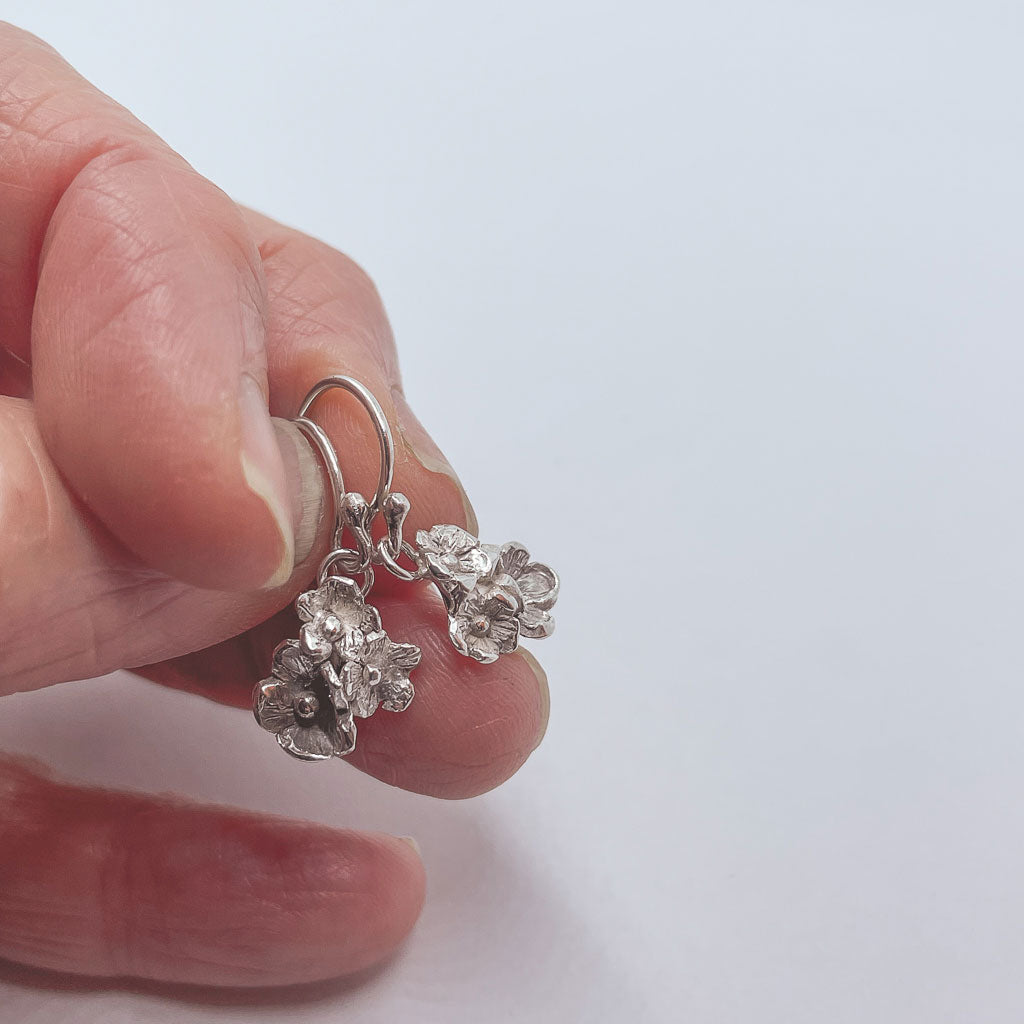 a hand holding a pair of silver flower dangle earrings