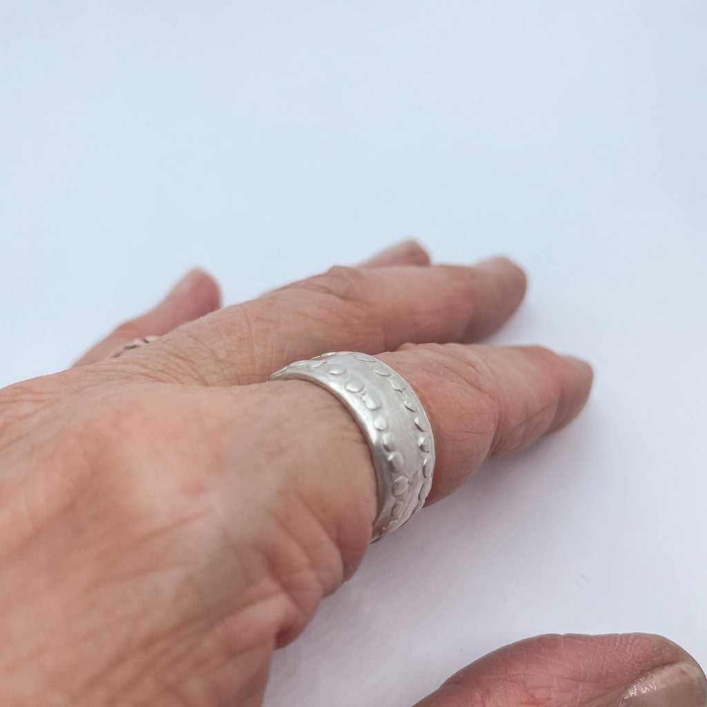 A hand wearing a Sterling Silver Unisex Ring with an organic texture creating a modern artefact