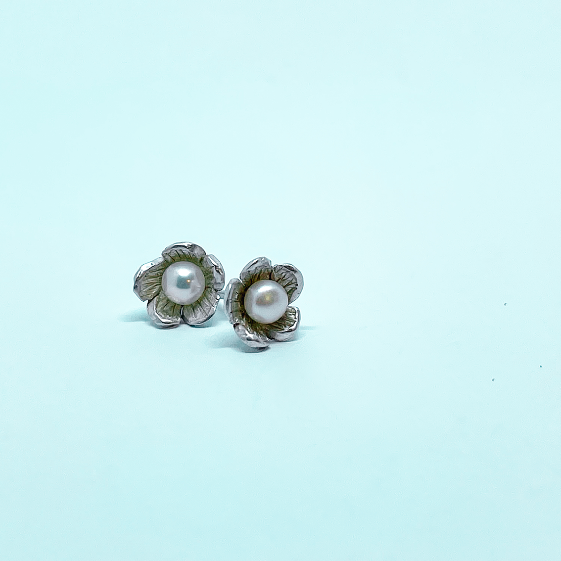 A close up of a pair of small flower Stud Earrings in Sterling Silver set with a white freshwater pearl