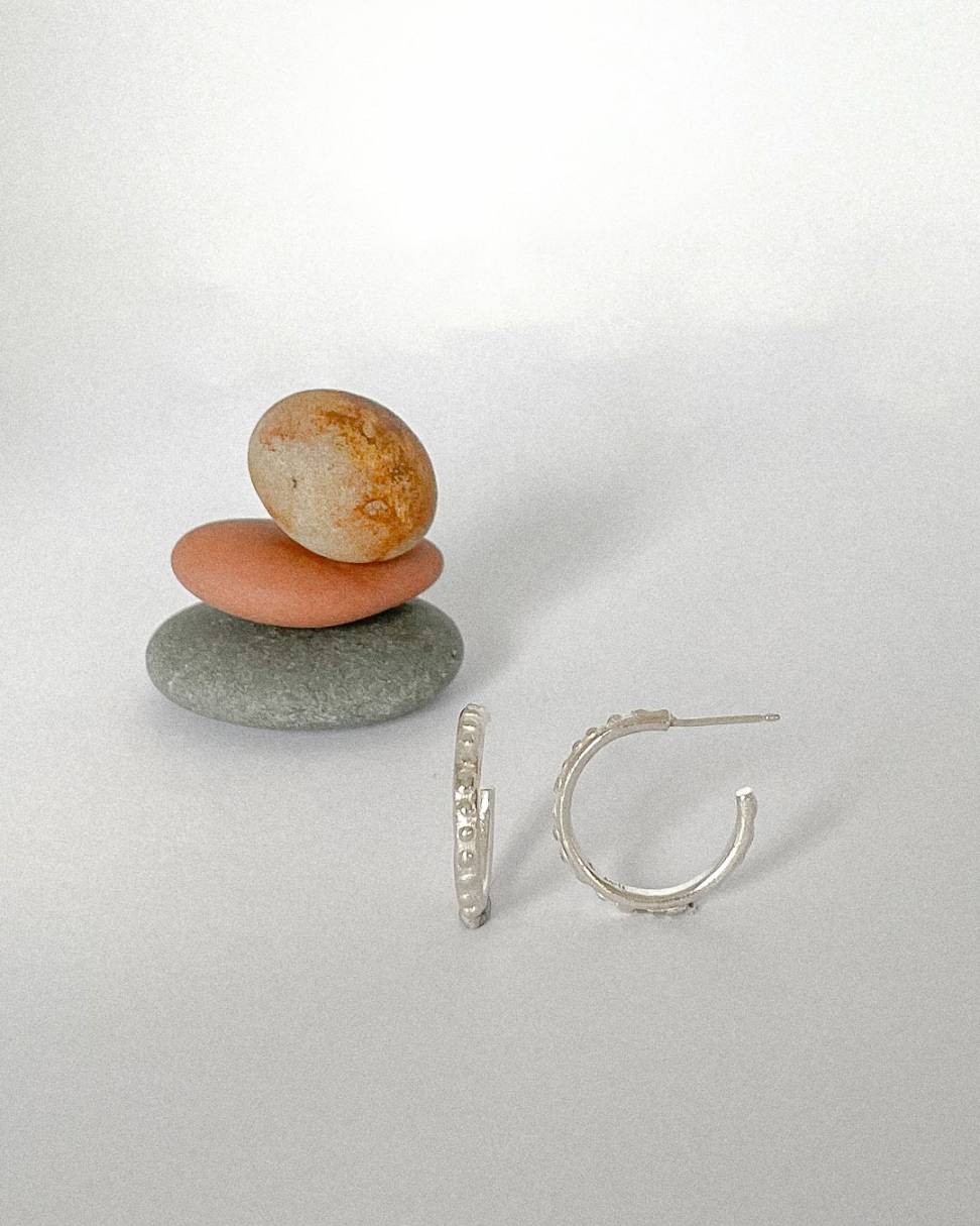 A pair of Hoop Earrings showing front and side profile in Sterling Silver standing in front of three balanced stones