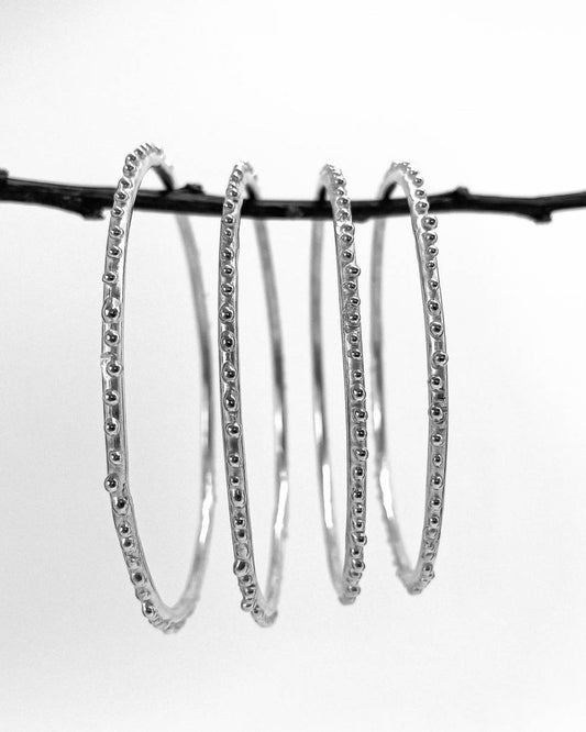 Four bangles with am organic textured surface in Sterling Silver hung from a branch in size order