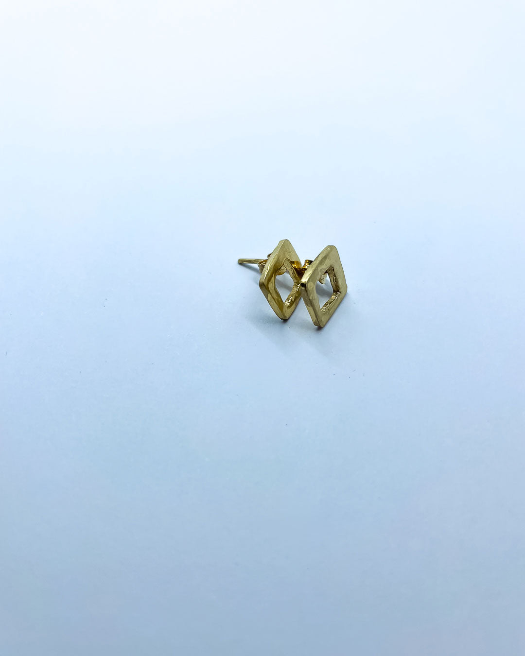 A side profile of a pair of Gold open geometric form pierced earrings inspired by Mid Century Geometric Patterns. Deliberately left to show makers marks.