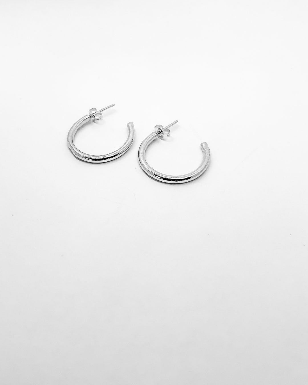 A pair of Sterling Silver Hoop earrings lying next to each other on a white surface