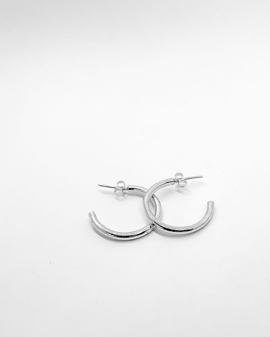 A pair of Sterling Silver Hoop earrings overlapping on a white surface