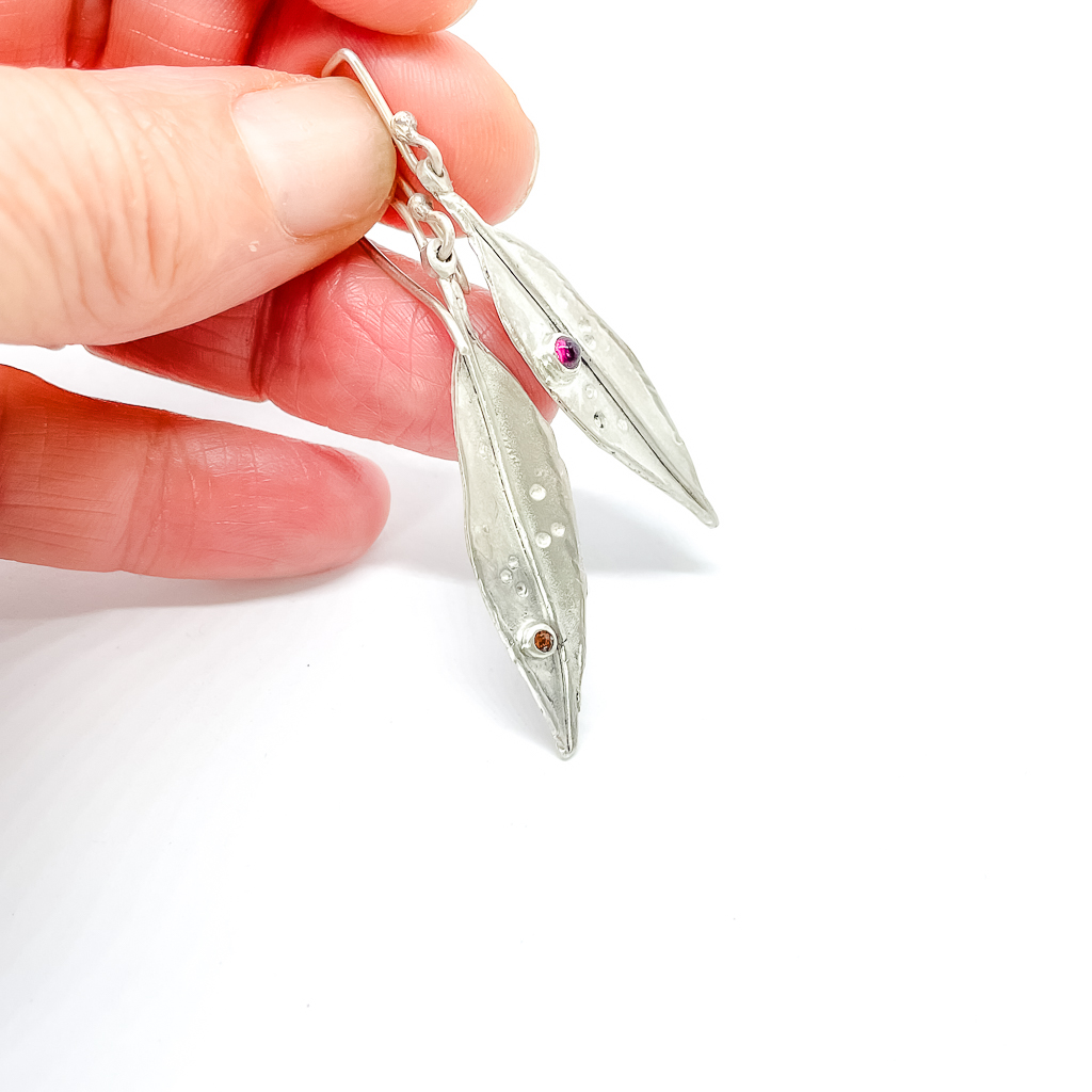 Hand holding a pair of Silver leaves set with gemstones