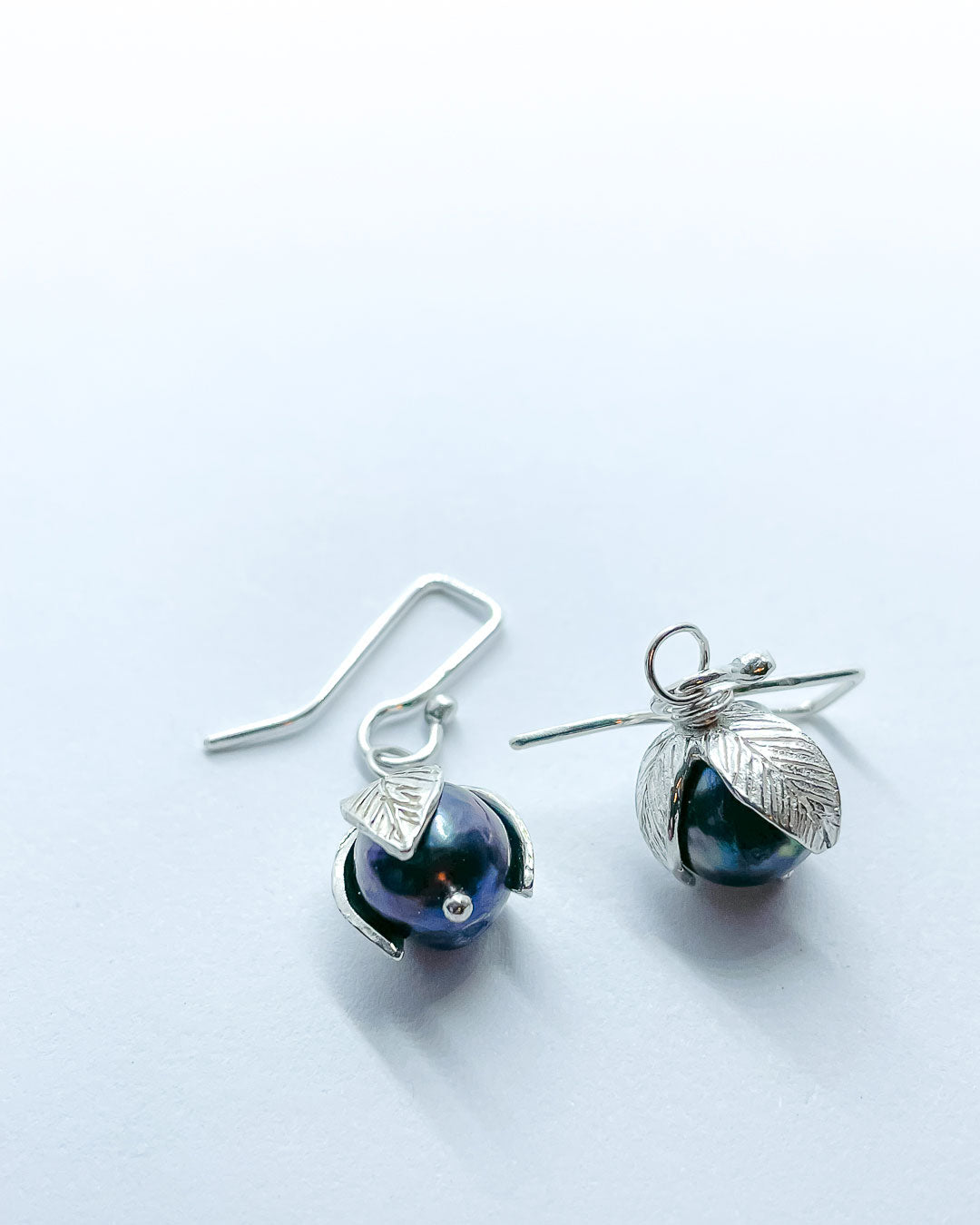 A pair of black pearls topped with Stylised leaves hung from artisan earring hooks