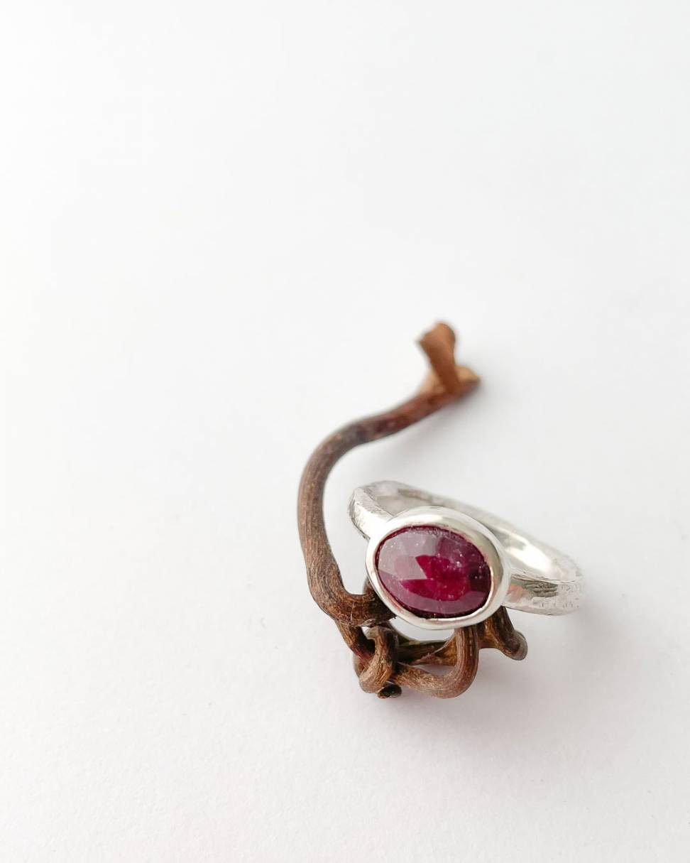 A close up of an organic Sterling Silver ring set with a large faceted oval ruby resting on a twisted vine
