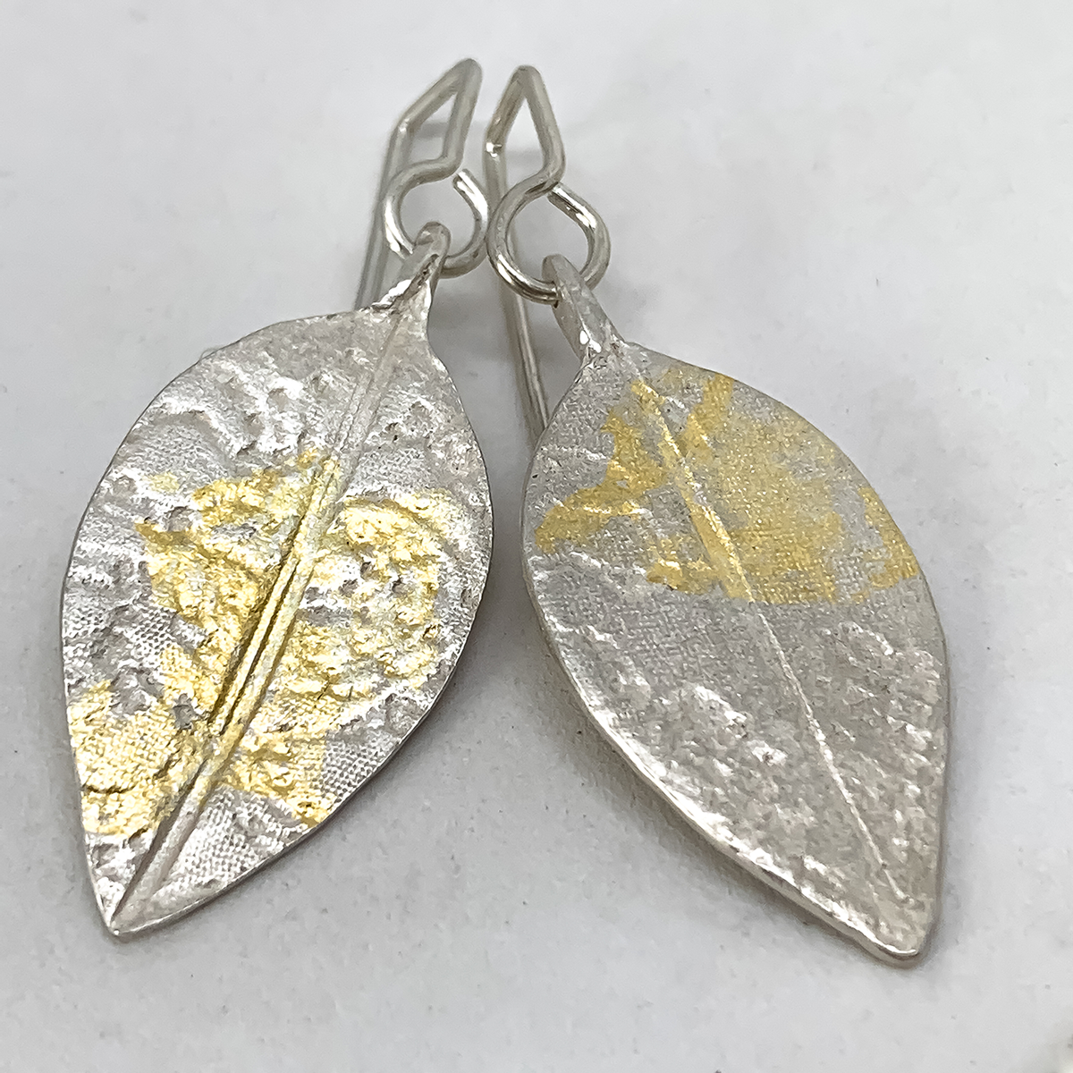 A pair of stylised leaf earrings with lace embossed into the surface and random patterns of 24ct Gold leaf applied like sunlight dappling the surface