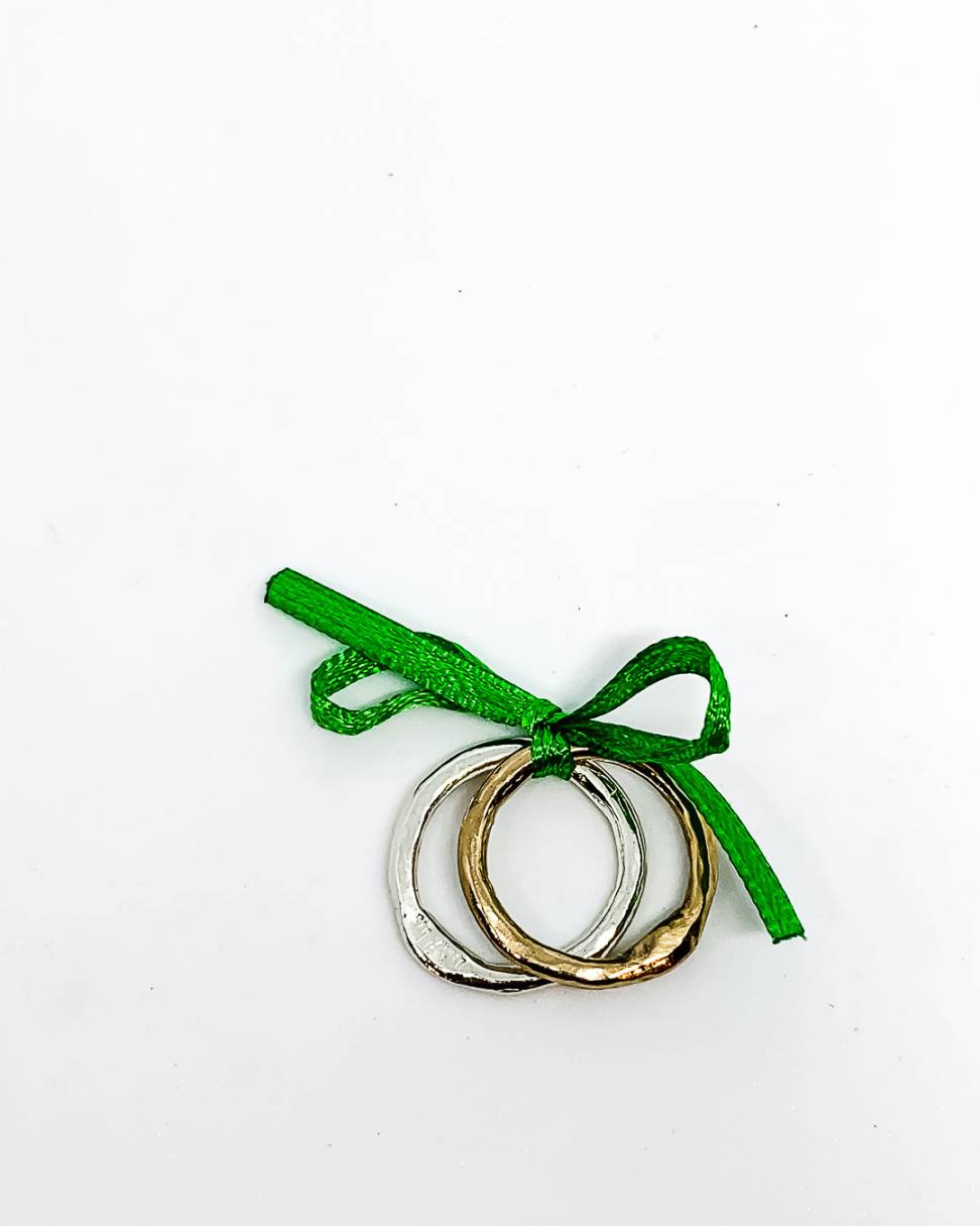 A pair of organic stacking rings one Sterling Silver and the other a golden bronze tied with a green ribbon