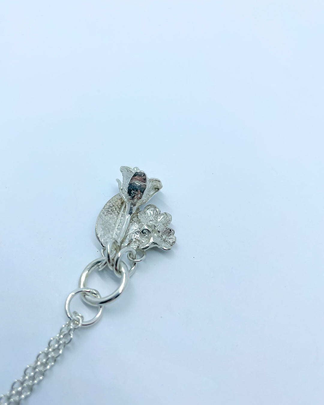 Three Sterling Silver Charms hung from a silver chain - the charms are a bouquet of flowers, a textured leaf and a freesia bloom