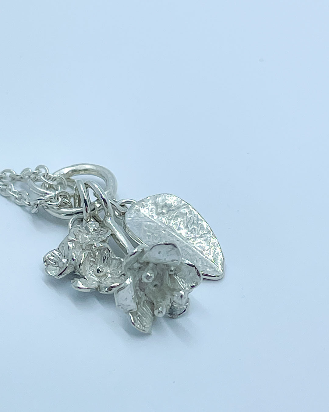 Three Sterling Silver Charms hung from a silver chain - the charms are a bouquet of flowers, a textured leaf and a freesia bloom