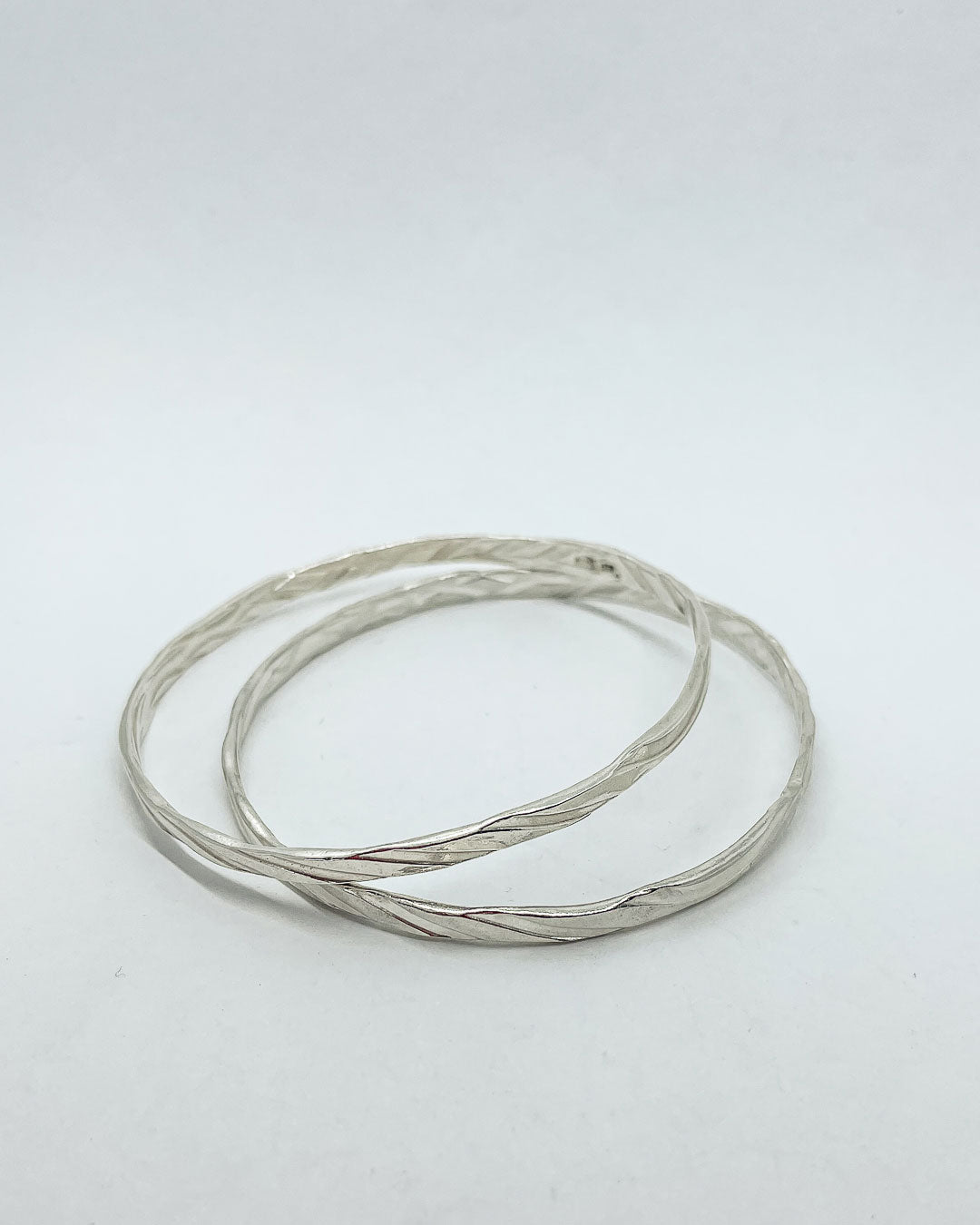 Two sterling Silver stacking bangles lying on the ground with a undulating texture on both the outside and inside of the band