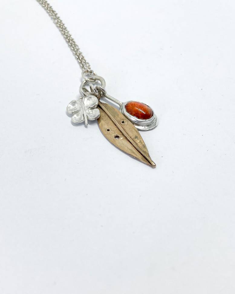 A summer garden charm necklace made of Sterling Silver and Bronze with a 8mm x 6mm beautiful Sunstone bezel set charm, a pohutukawa leaf charm and a 3d butterfly