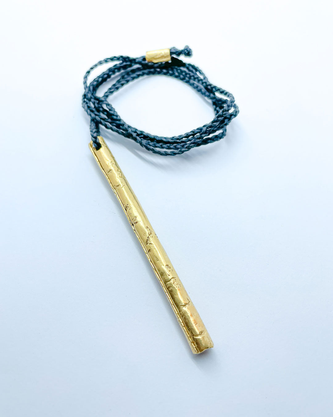 A gold pendant hung from a black plaited cord
