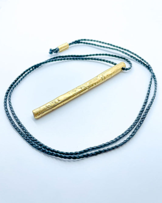 A gold pendant hung from a black plaited cord