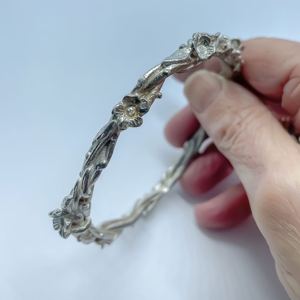 A hand holding a Sterling Silver Bangle formed from wrapped vines, leaves and flowers