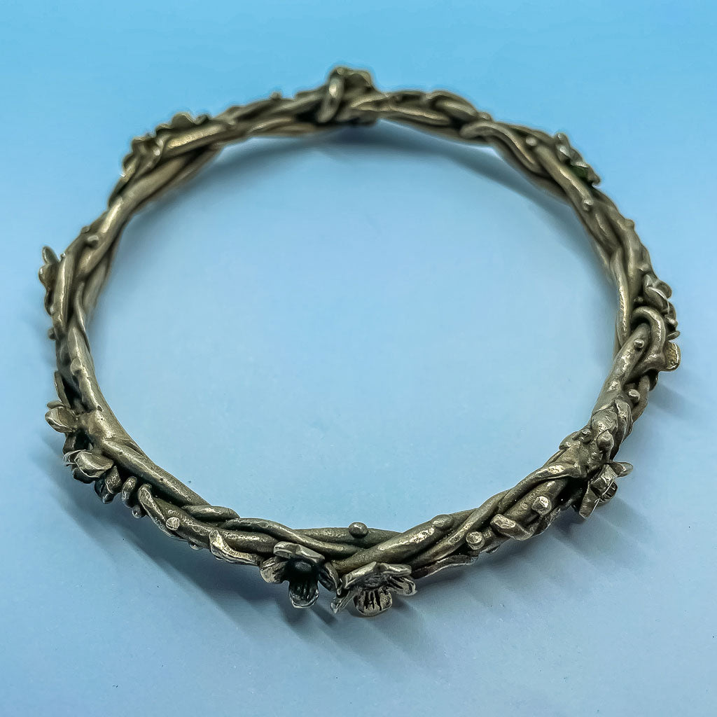 a bronze bangle formed from wrapped vines, leaves and flowers