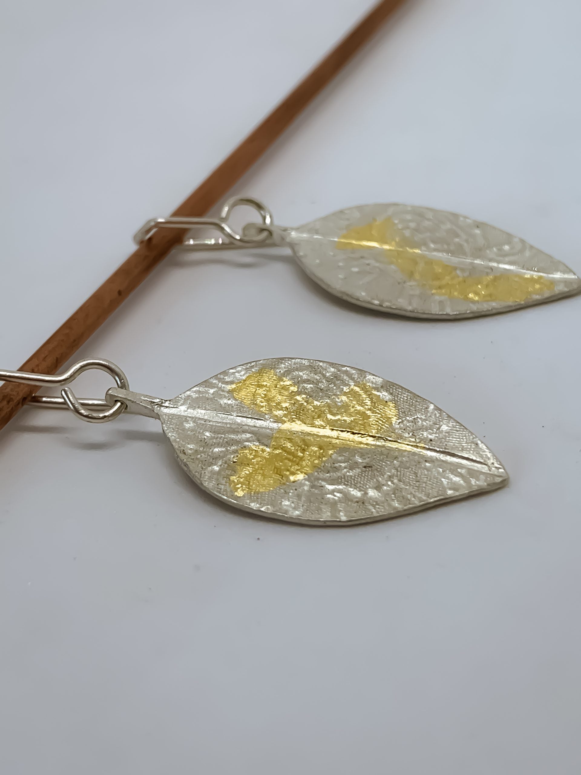 A pair of stylised leaf dangle earrings embosed with lace designs and patterns of 24ct Gold leaf applied