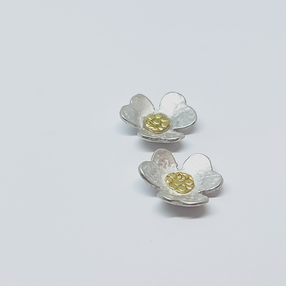 Close-up of Clover Stud Earrings in sterling silver with recycled 18ct gold centres, showing polished surface and soft flower form.