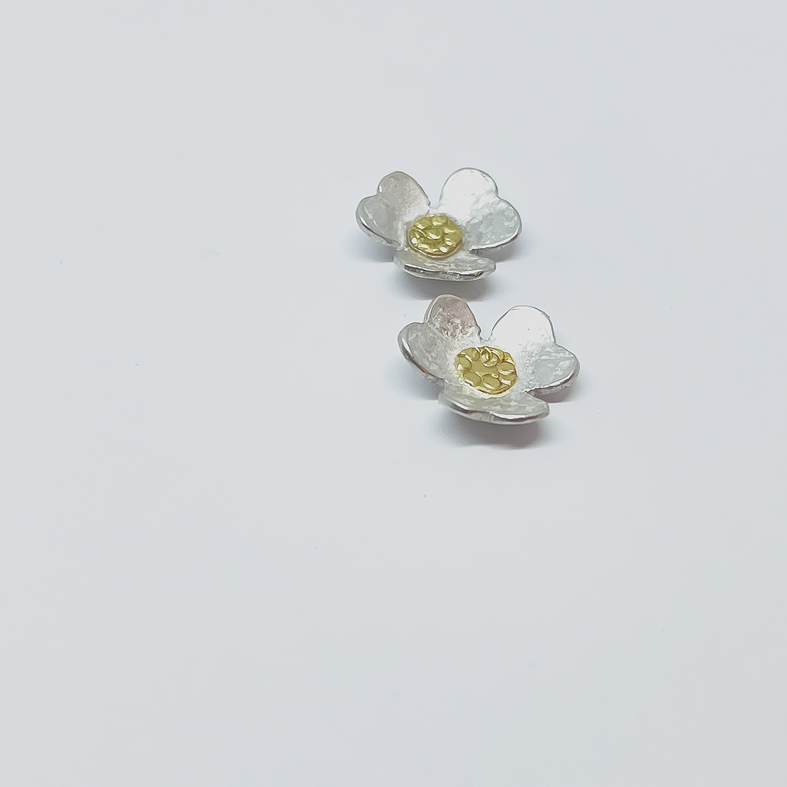 Angled from a top-down view of Clover Stud Earrings in sterling silver and gold, photographed from a distance to show the curve of the clover stud earring on a light grey background.