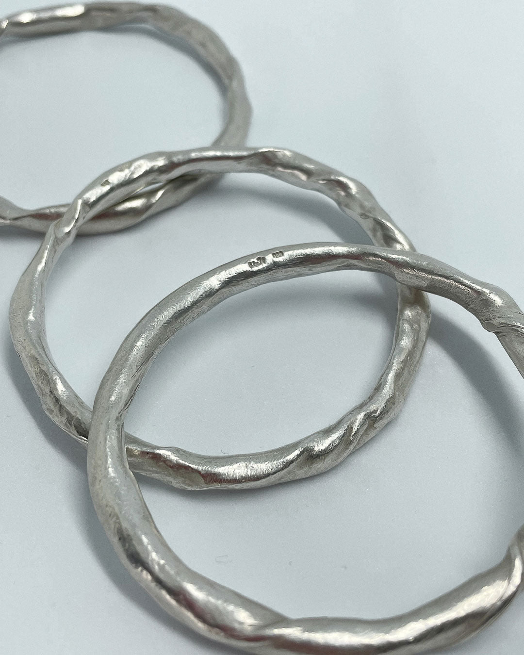 A close up of the makers marks for 3 heavy organic round Fine Silver Bangles lying on a flat surface