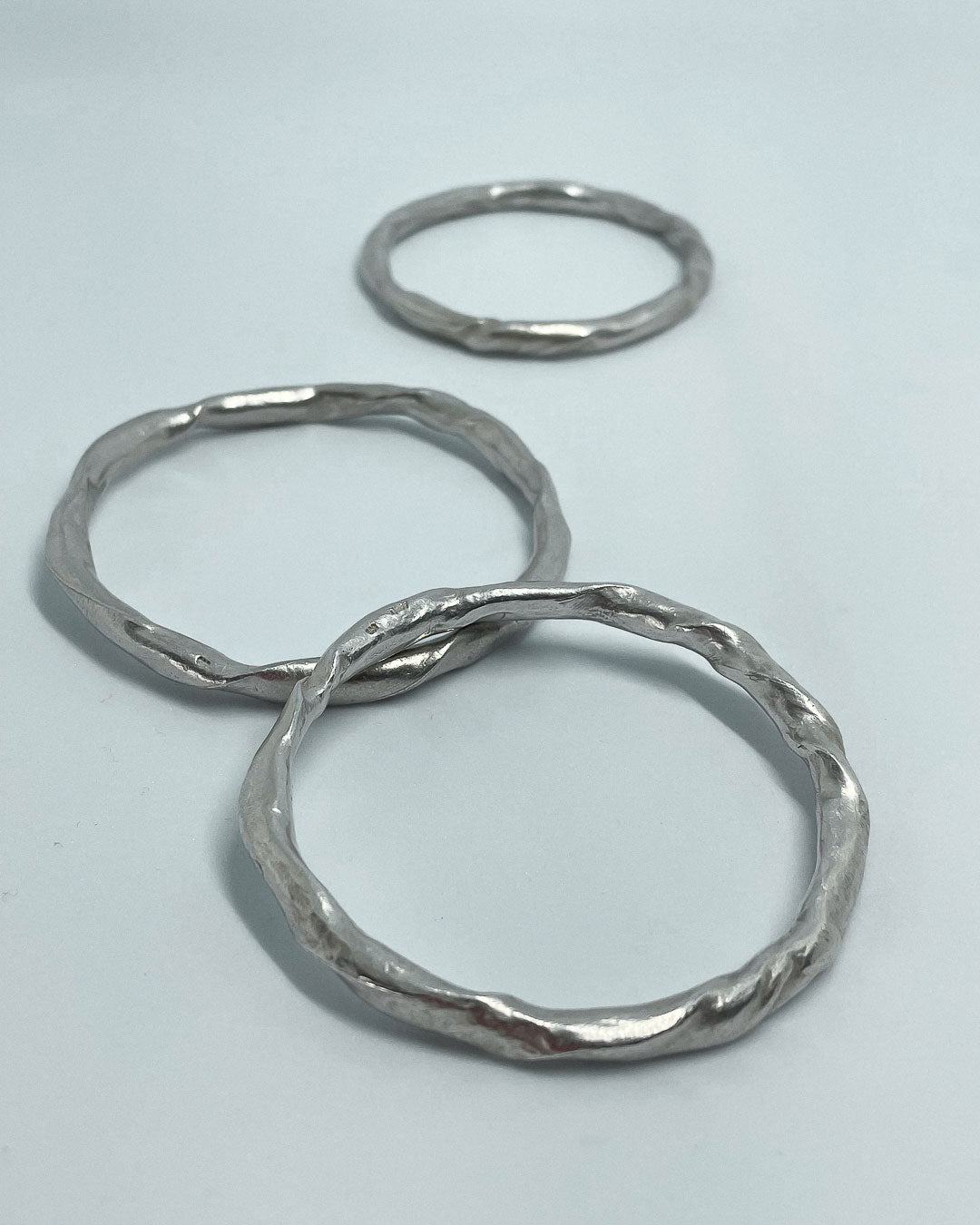 3 heavy organic round Fine Silver Bangles lying on a flat surface, two are stacked against each other