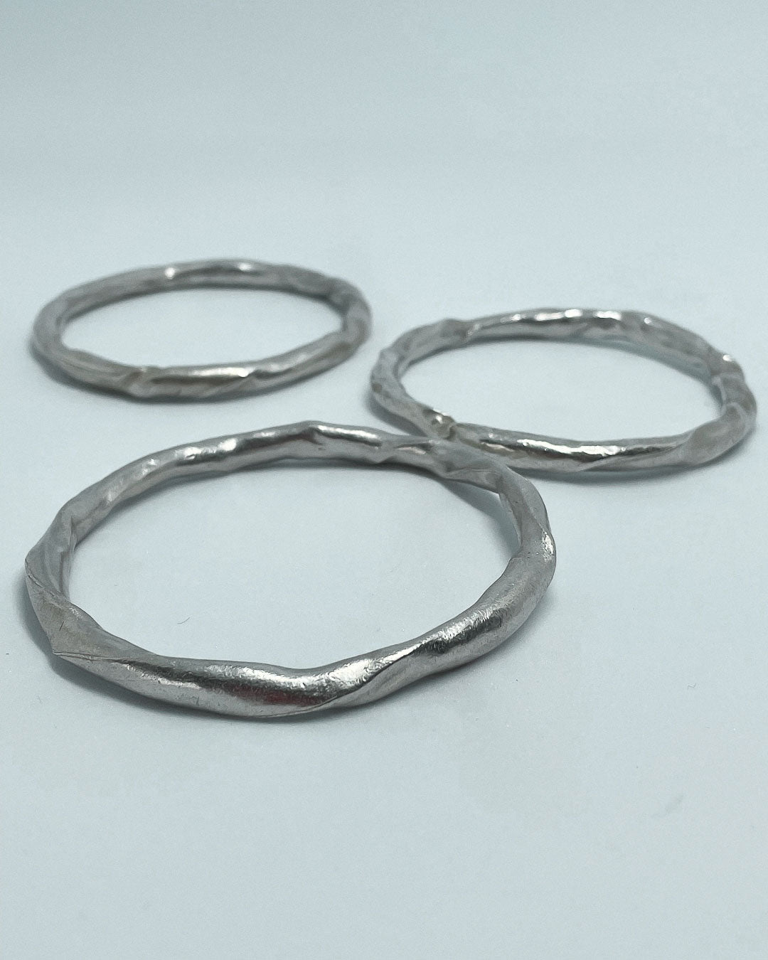 3 heavy organic round Fine Silver Bangles lying on a flat surface